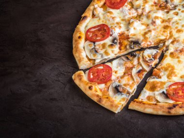 Mantarlı, domatesli ve peynirli bir dilim pizza koyu bir arka planda yatıyor. Pizzanın kalanının yanında dilimlenmiş bir dilim.