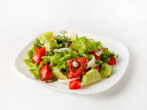 Salade van verse komkommers, tomaten en sla met uien en gehakte kruiden, een bord op een witte achtergrond — Stockfoto