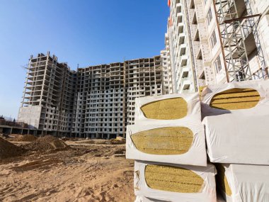 Duvarlar için birkaç paket yalıtım malzemesi yapım aşamasındaki yüksek katlı bir binanın arka planında kurulum için hazırlandı.