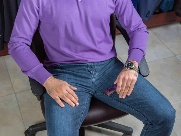 Um jovem de camisola roxa e jeans senta-se em uma cadeira no salão de uma loja de roupas — Fotografia de Stock
