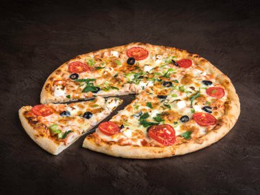 Tavuklu, peynirli, domatesli ve zeytinli lezzetli pizza koyu bir taş yüzeyde yatıyor.
