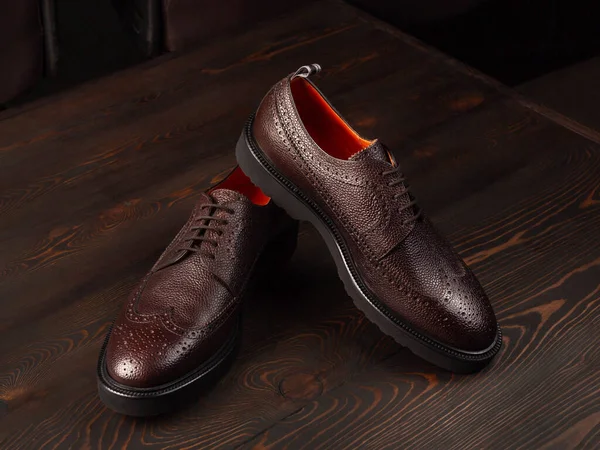 A pair of brown men\'s shoes made of genuine leather with an orange lining. Side view, close up. Background from brown boards. Selective focus