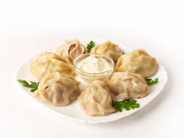 Bir porsiyon manti ile et ve bir kase ekşi krema, beyaz arka planda maydanoz yapraklarıyla süslenmiş.