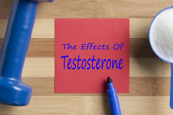 The Effects Of Testosterone written on note with sport supplement and dumbbell on wooden desk. Top view.