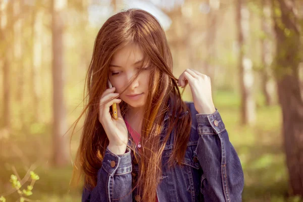 La chica con el pelo largo y liso castaño en una chaqueta de mezclilla habla o —  Fotos de Stock