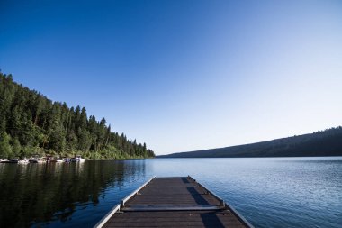 Wooden dock extends over placid mountain lake clipart