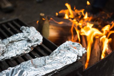 Tin foil dinners cooking on a metal grill over campfire clipart