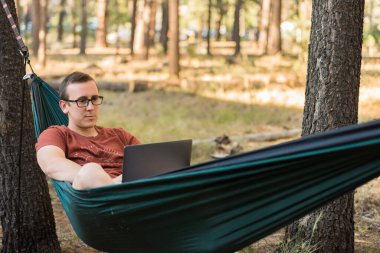 Uzak bir yerde kamp yaparken internet veya dizüstü bilgisayar kavramı, hamakta gri dizüstü bilgisayar