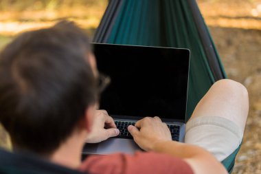 Uzak bir yerde kamp yaparken internet veya dizüstü bilgisayar kavramı, hamakta gri dizüstü bilgisayar