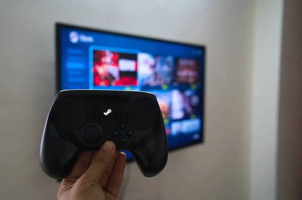 man with a controller standing in front of a PC console TV screen with a  steam controller playing popular free to play game Roblox Stock Photo -  Alamy