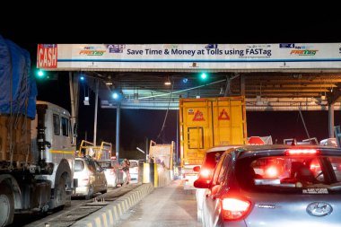 FASTag ve Paytm 'dan bahseden büyük beyaz bir yatak başı, NHAI gişesinde bekleyen araçların gece görüntüsü.