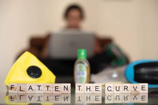 Wooden blocks with flatten the curve with an out of focus background of a young indian girl woman working on her phone laptop — Stock Photo, Image