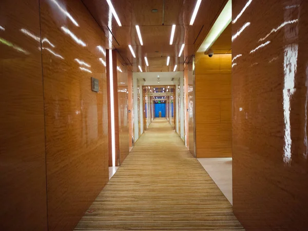 Gurgaon India, Circa 2020 - Photograph of a long beautifully decorate wooden corridor with carpeted floor and rooms on both the sides. The corridor is brightly lit with a window at the end.