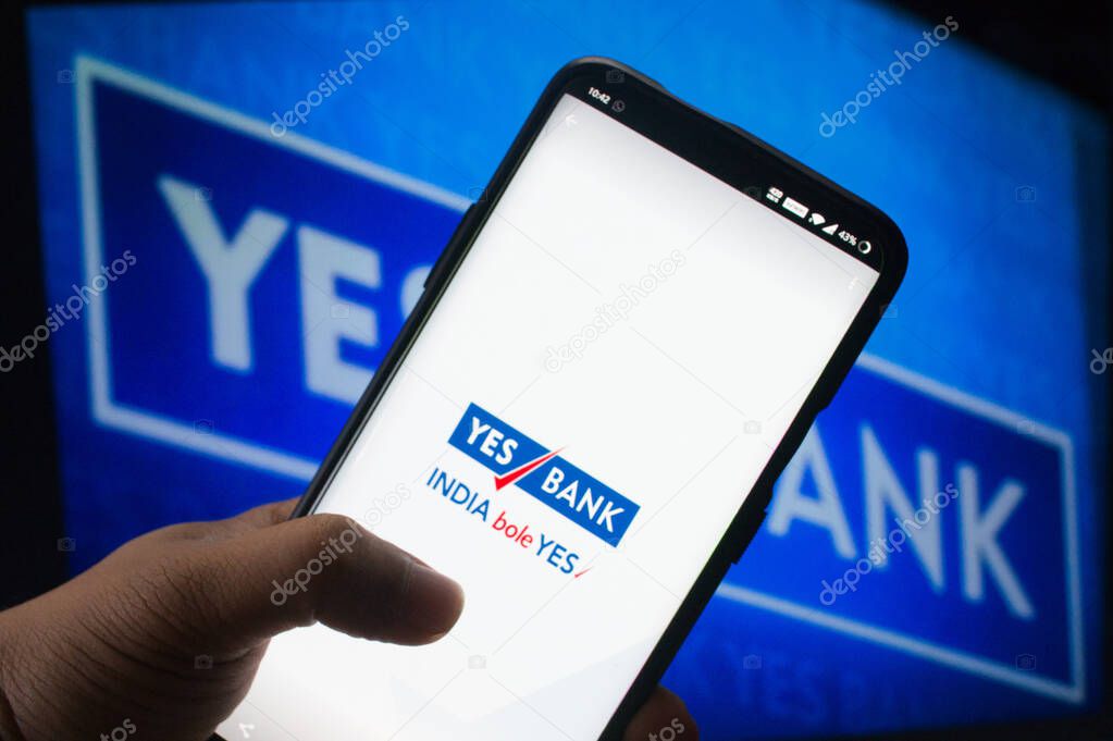 Jaipur, India, Circa 2020 - A mobile logged into the yes bank mobile application infront of the yes bank board. The background board is brightly lit. The screen shows the mobile application logging in.