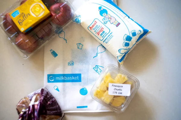 Flatlay image of multiple home essentials like milk, butter, fruits and bread coming from a milkbasket bag which provides a daily subscription delivery of groceries — Stock Photo, Image