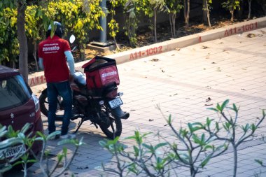 Zomato teslimatçısı kırmızı tişörtlü Zomato teslimat çantalı bisikletinin yanında bekliyor.