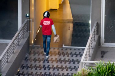 Zomato teslimatçısı, kırmızı tişörtlü ve Hint e-com şirketinden eve yemek getirmek için bir çanta taşıyor.