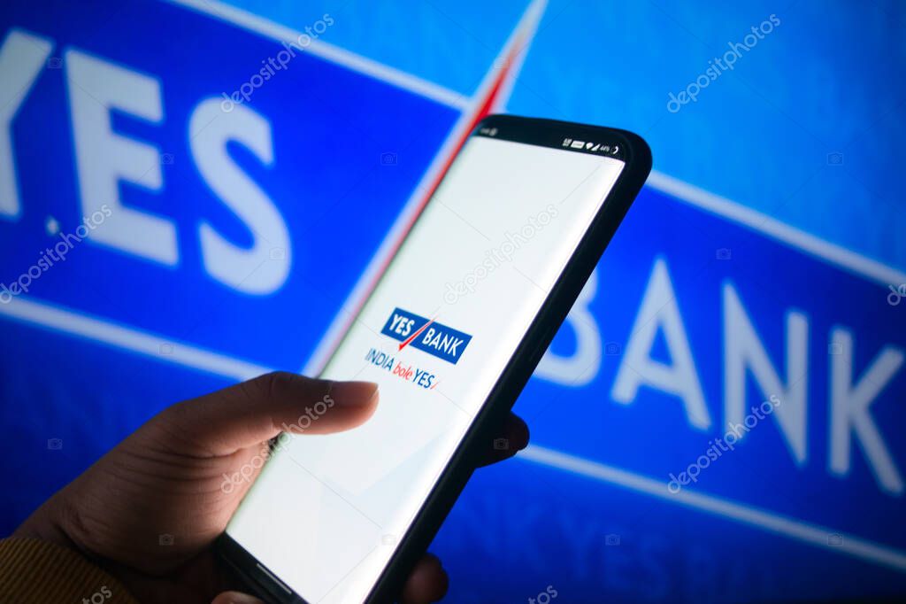 Jaipur, India, Circa 2020 - A mobile logged into the yes bank mobile application infront of the yes bank board. The background board is brightly lit. The screen shows the mobile application logging in.
