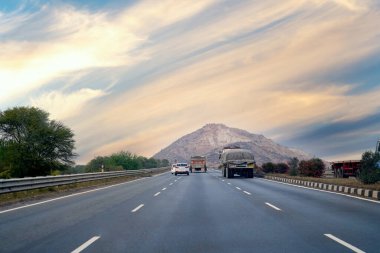 Uzaktaki dağa giden uzun düz yolu olan kamyonları ve arabaları olan boş Hint otoyolu.