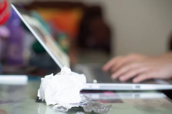 Young indian woman working on a laptop while sick with white tissues and medicine in silver foil nearby while she types in the background working on a project to safegurard her job and livelihood