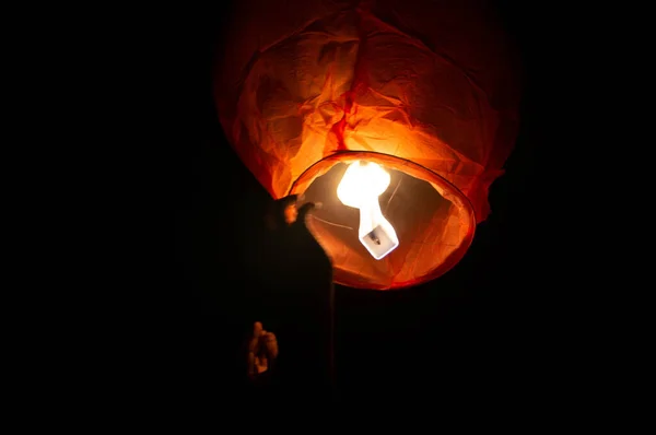 A red coloured sky lantern with the flames showing clearly lifiting off — Stock Photo, Image