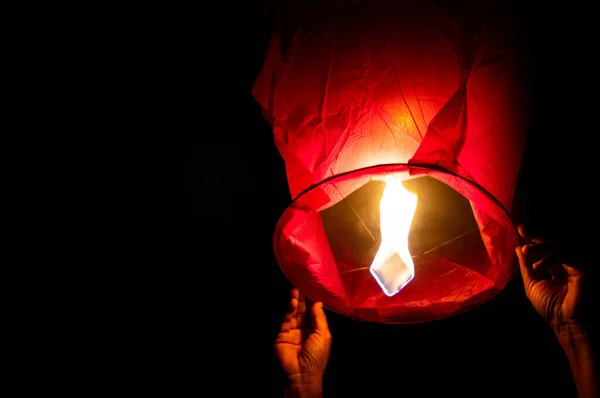 Person holding a red sky lantern with the flames showing clearly