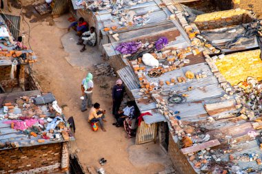 Delhi, Hindistan - 2020 dolaylarında: Surat maskesi takan insanların gecekondu evlerinin dışında oturdukları hava görüntüleri. Teneke çatılı tuğla evler etrafı pislik dolu dengesiz yapılardır.