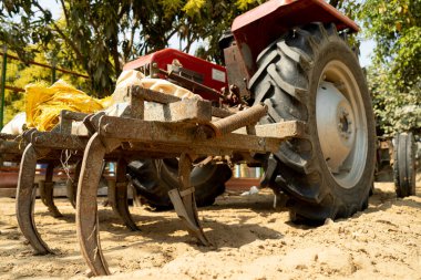 Kırmızılı bir traktörün arkasına ekin ekmek için yapıştırılmış paslı eski saban. Hindistan tarımının ülkenin artan nüfusunu beslemek için eski çağdışı ekipmanlara ne kadar bağlı olduğunu gösteriyor.