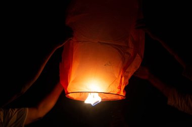 Kırmızı bir gökyüzü feneri tutan birinin fotoğrafı. Alevler açıkça görülüyor. Gökyüzü feneri havalanmasını bekleyen biri tarafından tutulur. Bu genelde Diwali, Makar Sankranti gibi özel durumlarda yapılır.