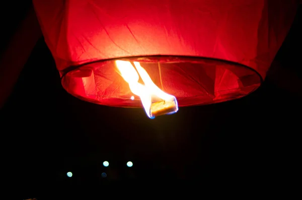 Photograph of a red sky lantern with the flames showing clearly lifting off to the sky. This is often done on special occassions like Diwali, makar sankranti