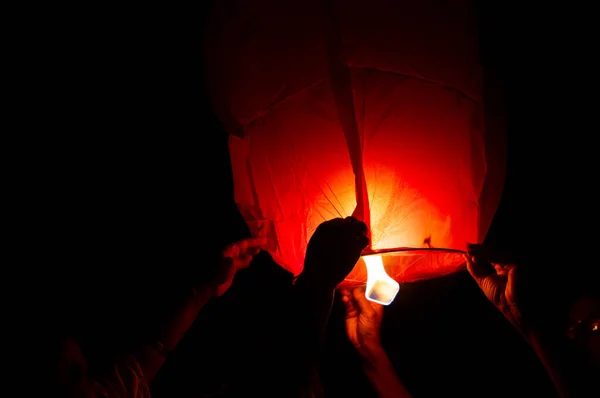 Photograph of a person holding a red sky lantern with the flames showing clearly. The sky lantern is held by a person waiting for it to lift off. This is often done on special occassions like Diwali, makar sankranti