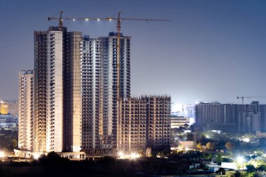 İnşaat binalarının altındaki havadan çekilen görüntüler üstten aydınlatılıyor ve üstünde vinç var. Hindistan 'ın Gurgaon Delhi gibi şehirlerindeki inşaat projelerini gösteriyor. Büyük konutlar ve ofis binaları geliyor.