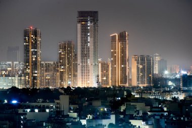 Çok katlı çok katlı gökdelenler geceleyin Gurgaon delhi 'de gece ön planda küçük evler ile aydınlandı. Kirliliğin olmadığı bir günde emlak, ofis ve konutlarla emlak sektörünün hızla geliştiğini gösteriyor