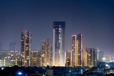 Çok katlı çok katlı gökdelenler geceleyin Gurgaon delhi 'de gece ön planda küçük evler ile aydınlandı. Kirliliğin olmadığı bir günde emlak, ofis ve konutlarla emlak sektörünün hızla geliştiğini gösteriyor