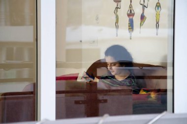 Camdan çekilen genç Hintli kız, koronavirüs salgını sırasında karantinada yalnız başına oturduğunu ve sosyal mesafeyi ölçtüğünü gösteriyor.