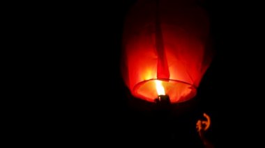 Kırmızı bir gökyüzü feneri uçuran ve alevleri açıkça görünen birinin videosu. Gökyüzü feneri havalanmasını bekleyen biri tarafından tutulur. Bu genelde Diwali, Makar Sankranti gibi özel durumlarda yapılır.