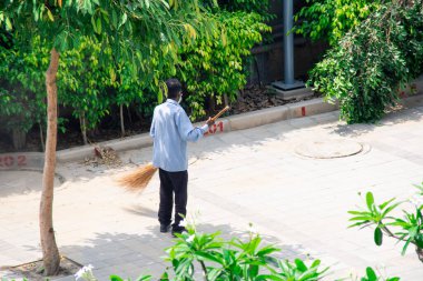 Mavi üniformalı bir temizlikçi, uzun süpürgeli kaldırımlar ve bir toplumda uzun bir süpürge ile Corona covid19 'un temizlik ve sterilizasyonunun bir parçası olarak.