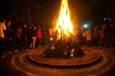 Gurgaon, Hindistan, Circa 2020 - Lohri, Holi veya Holika Dahan 'ın uğurlu festivali için yakılan dev bir şenlik ateşinin fotoğrafı. Ateş festivalin tadını çıkaran insanlarla çevrili. Bu, Hindistan 'da kızartılmış bir bahar hasat festivali.