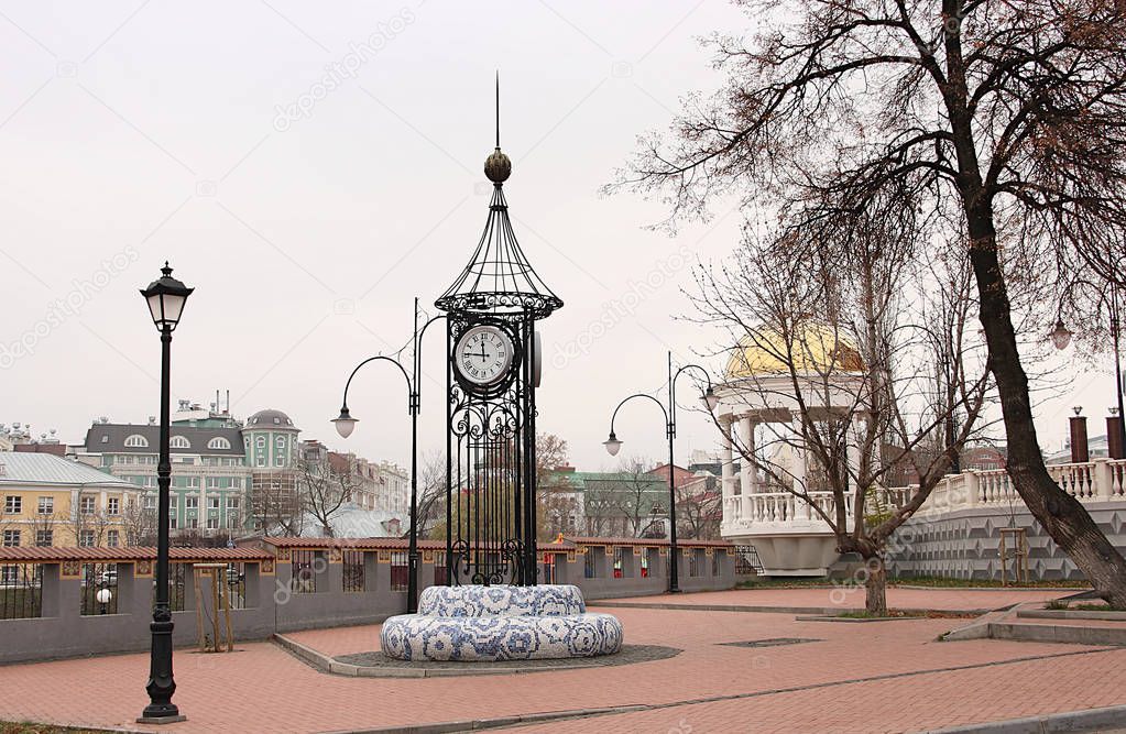 Clock in the park on the background of old and new buildings of the city