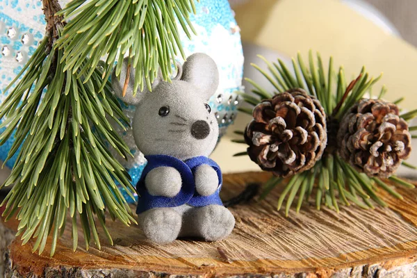 Christmas mouse toy in a blue vest on a background of a blue ball and a pine branch with cones