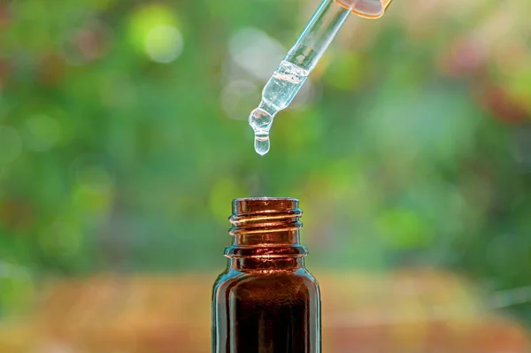 Güzellik merkezi konsepti. Şişeye damlayan bitkisel masaj yağı. Esans damlası ve şişeyle Pipette, bulanık doğa arka planına yakın çekim. Seçici odak
