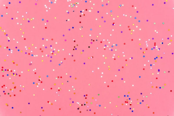 Pembe modaya uygun arka planda ışıldayan çok renkli yıldızların fotoğrafı. Projeleriniz için şenlikli tatil geçmişi. Kutlama konsepti. Noel deseni. Üst manzara, düz uzanma