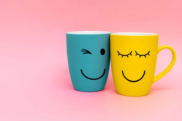 Valentine\'s day concept. Two happy cups yellow and turquoise colors on pink background. Happy friday word concept. Simbol of love and relationship. Copy space