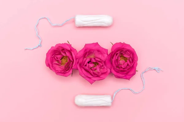 Komposition von oben mit rosafarbenen Blüten und zwei Tampons auf pastellrosa Hintergrund. Frauen kritische Tage und Zeitraum Konzept. flache Lage, Kopierraum, selektiver Fokus — Stockfoto