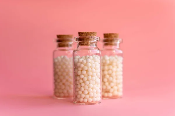 Homeopatik küreselerin yakın plan görüntüsü cam şişelerde, pastel pembe arka planda. Alternatif homeopati ilaç, sağlık sigortası ve hap konsepti. Seçici odak