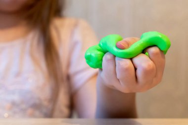 Yeşil balçık tutan bir kızın eli. Sümük yakın planda. Çocuk sümük oynuyor, geriyor. Yapışkan olmayan ezici kitle şeklinde ev yapımı çocuklar için yaratıcı bir oyuncak. Seçici odak