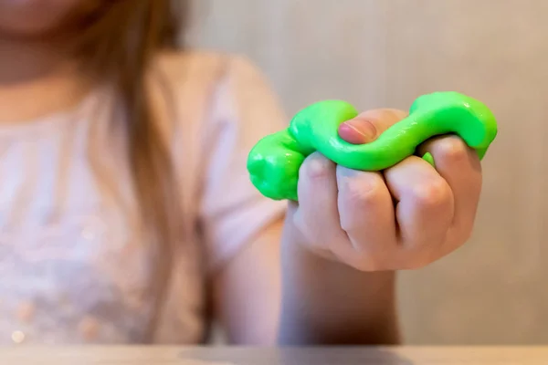 Yeşil balçık tutan bir kızın eli. Sümük yakın planda. Çocuk sümük oynuyor, geriyor. Yapışkan olmayan ezici kitle şeklinde ev yapımı çocuklar için yaratıcı bir oyuncak. Seçici odak