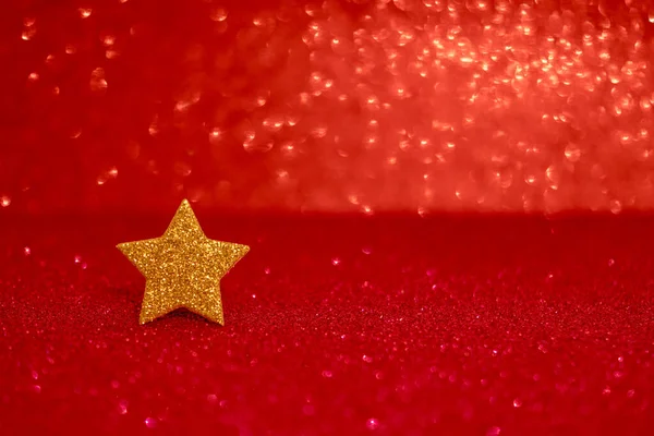 Golden glittering star on red glitter background. Festive abstract red glitter texture background with single golden star. Selective focus, copy space