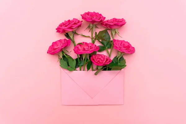 Tatil konsepti. Pembe arka planda pembe zarf içinde pembe güller. Model yap, düz yat, üst görünüm, kopyala alanı. Düğün davetiyesi ya da aşk mektubu. Sevgililer Günü ya da diğer tatil kavramları.