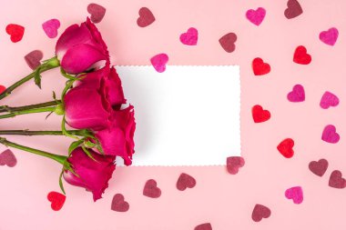 Çiçek kompozisyonu. Pembe gül çiçekleri ve yumuşak pembe arka planda kalp şeklinde kağıt konfeti ve metin için kağıt kart notu. Tatil geçmişi. Düz konum, üst görünüm, kopyalama alanı